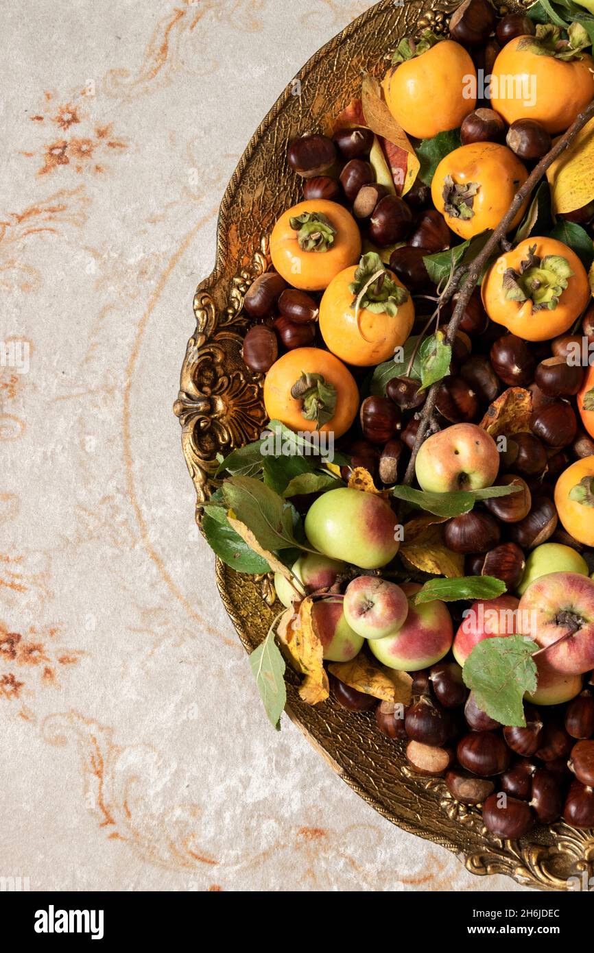 Plat de fruits d'automne.Pommes fraîches, kaki et châtaignes sur un plateau doré Banque D'Images