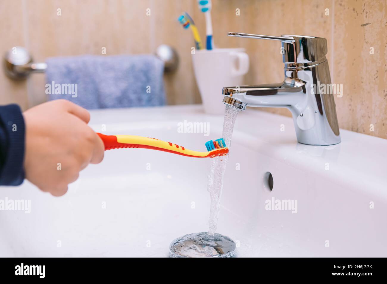 Détail du bras d'une petite fille dans la salle de bains, versant de l'eau sur sa brosse à dents dans le lavabo.Concept de brossage des dents, d'hygiène et d'enfance. Banque D'Images