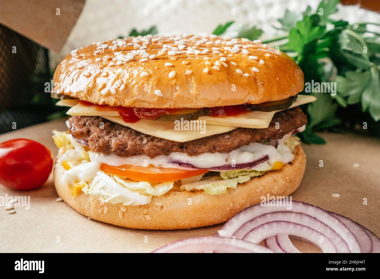 Double hamburger classique avec côtelette de viande, laitue, tomate, concombre mariné, fromage,oignon et sauce sur papier artisanal avec tomates cerises et parsl vert Banque D'Images