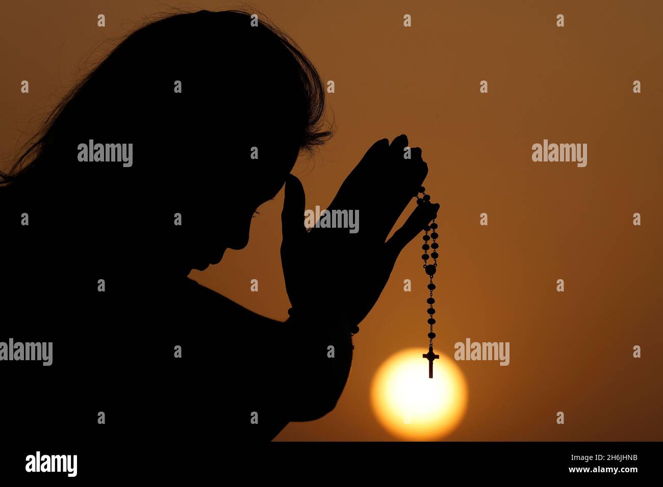 Silhouette de femme fidèle priant avec des perles rosaires au coucher du soleil comme concept de religion, de foi, de prière et de spiritualité, Dubaï, Émirats arabes Unis Banque D'Images