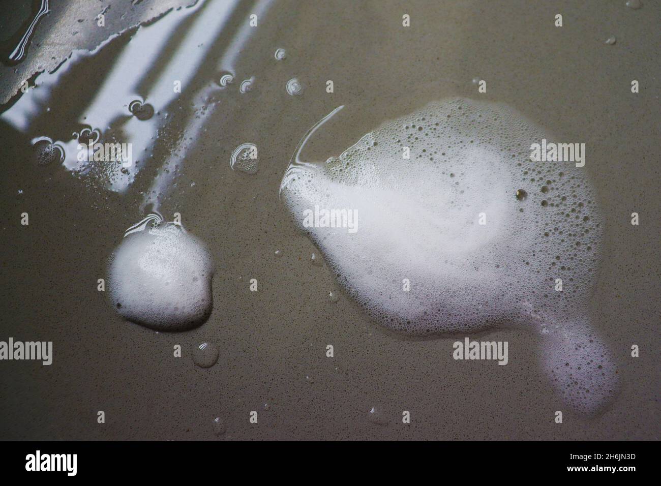 Gros plan de la mousse de savon avec bulles à travers le dessus de la cuisine, pendant le lavage de vaisselle, avec réflexion de la lumière de fenêtre. Banque D'Images