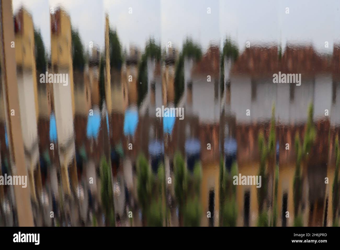 Vue abstraite vue à travers une fenêtre en verre nervuré, montrant un paysage fragmenté non défini avec des maisons et des arbres. Banque D'Images