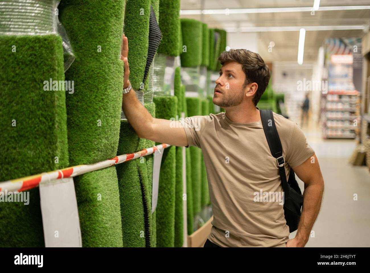 Homme décontracté vérifiant la qualité de l'herbe artificielle en rouleau tout en touchant le matériau et en regardant vers le haut au centre Banque D'Images
