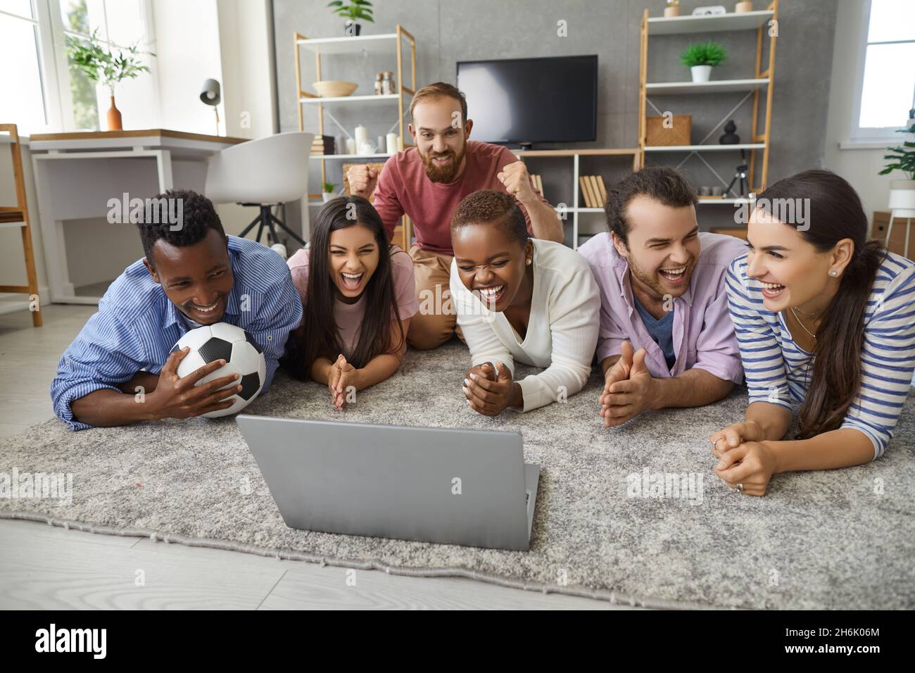 Amis heureux divers groupe regardant un match de football sur un ordinateur portable couché sur le sol Banque D'Images