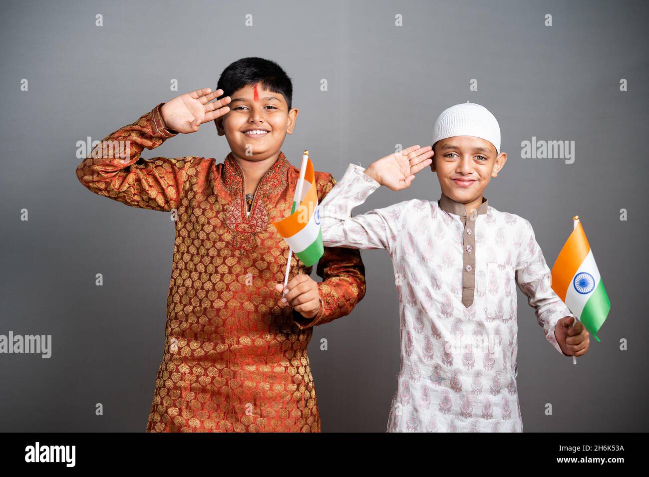 Enfants musulmans hindous saluant en tenant le drapeau indien sur fond gris - concept d'enfants célébrant la République indienne ou jour de l'indépendance, religieux Banque D'Images