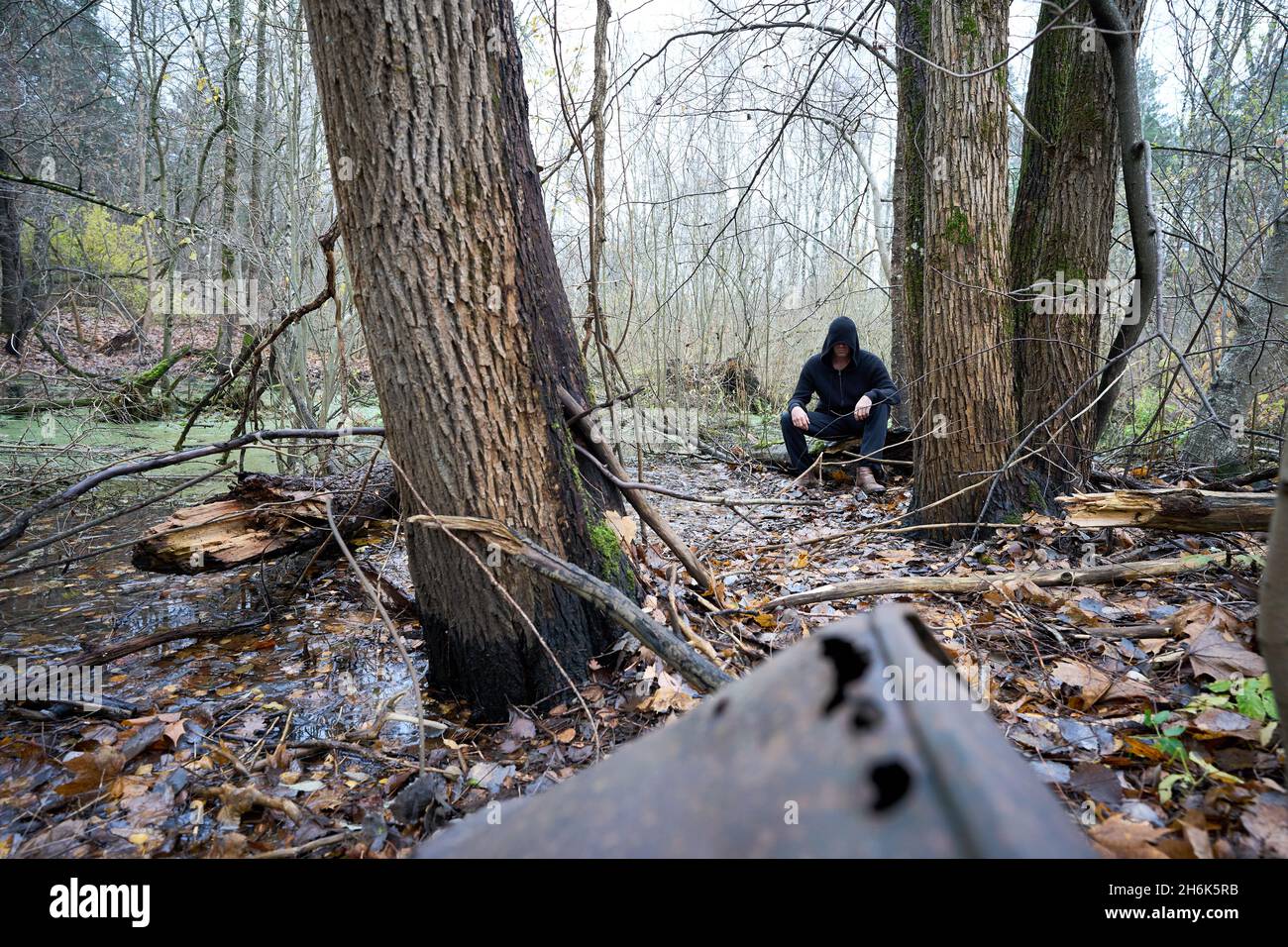 Une personne dans le sweat à capuche noir assis sur le marais dans la forêt d'automne.Ancien baril rouillé à l'avant.Costume Assassin cosplay. Banque D'Images