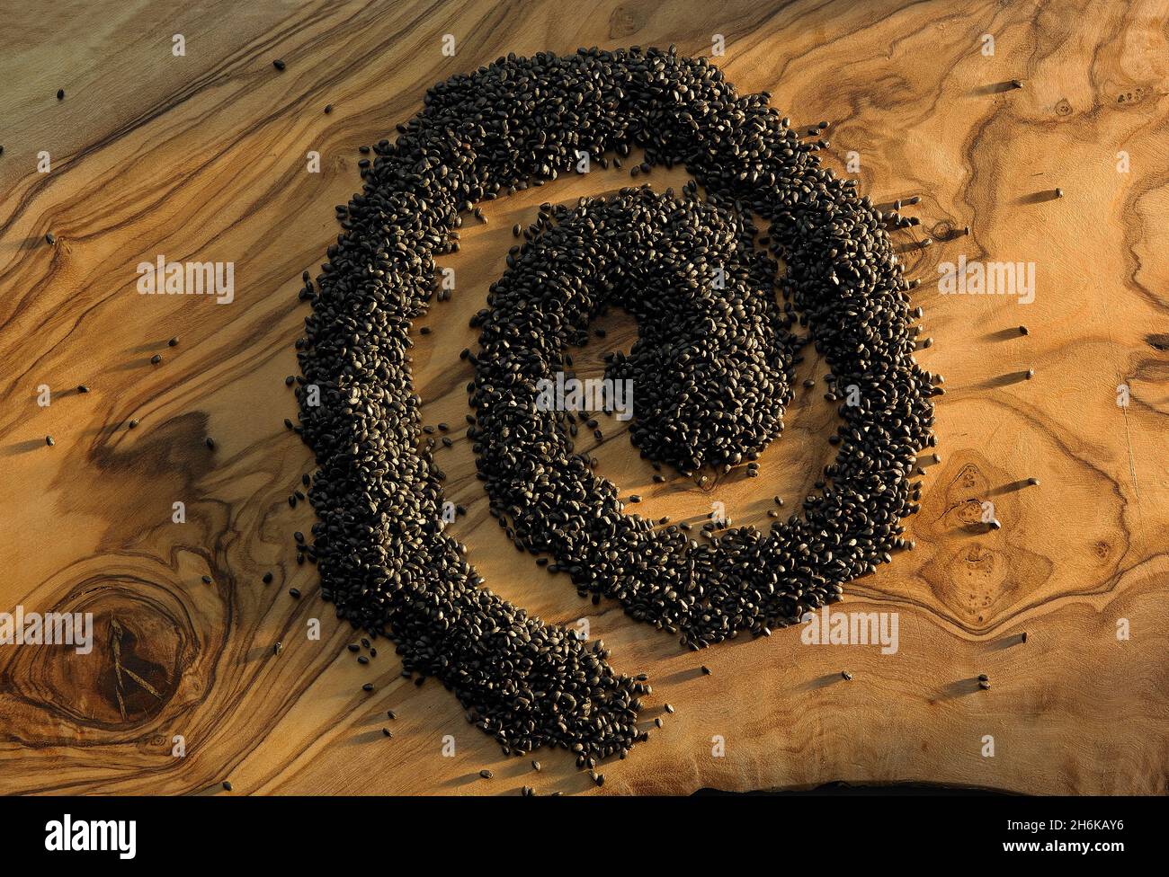 Graines noires formant une spirale sur une planche à découper en bois Banque D'Images
