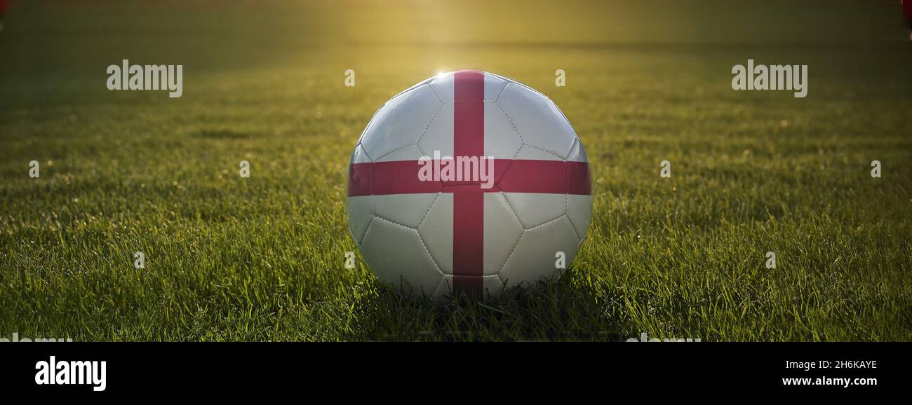 Ballon de football blanc avec croix d'Angleterre imprimée sur le terrain, sur le terrain de football, avec le soleil brillant de derrière et réfléchissant sur la surface du football. Banque D'Images