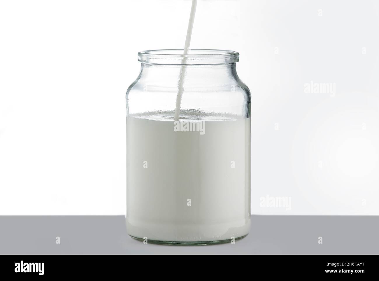 Bol transparent sur table grise et fond blanc rempli de lait frais par le dessus. Banque D'Images