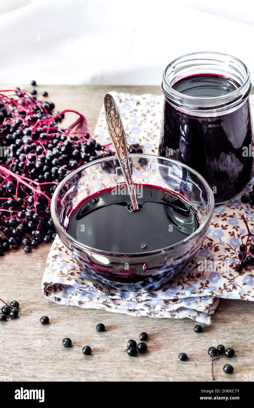 Sirop de sureau noir fait maison dans un bol en verre et un pot et des petits pains de sureau noir en arrière-plan Banque D'Images