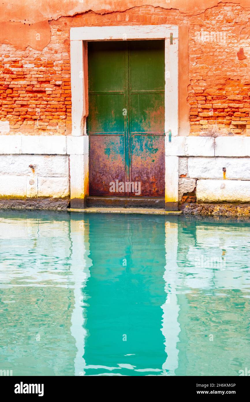 Vieille porte fermée menant au canal avec une étonnante réflexion turquoise dans l'eau Venise Italie Banque D'Images