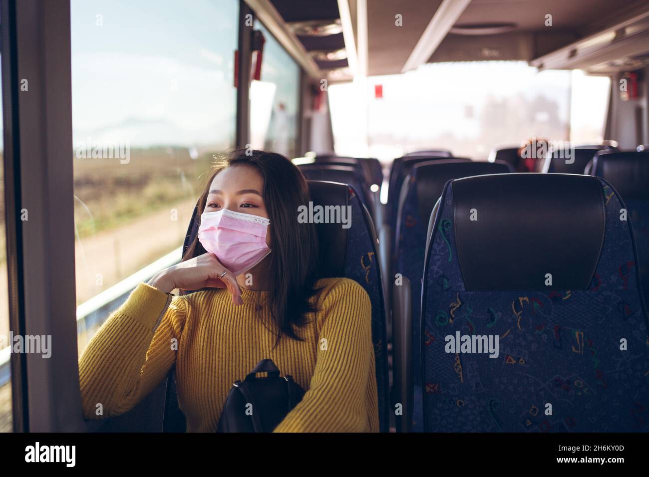 Jeune asiatique jolie femme voyageant dans un bus vide avec masque rose pendant la journée Banque D'Images