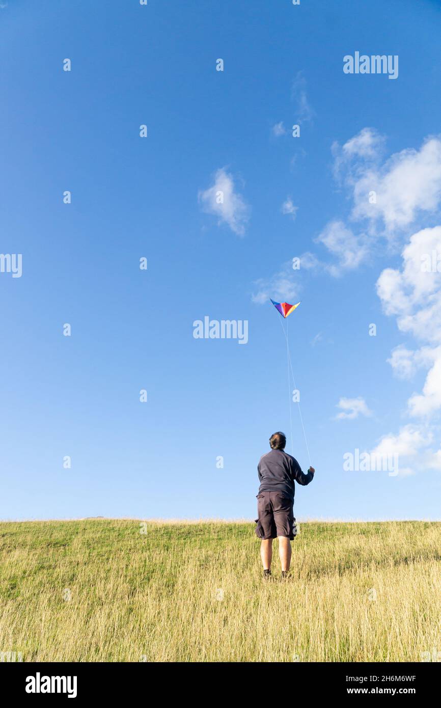 Homme volant un cerf-volant sur une colline en été, entouré par le ciel bleu Banque D'Images