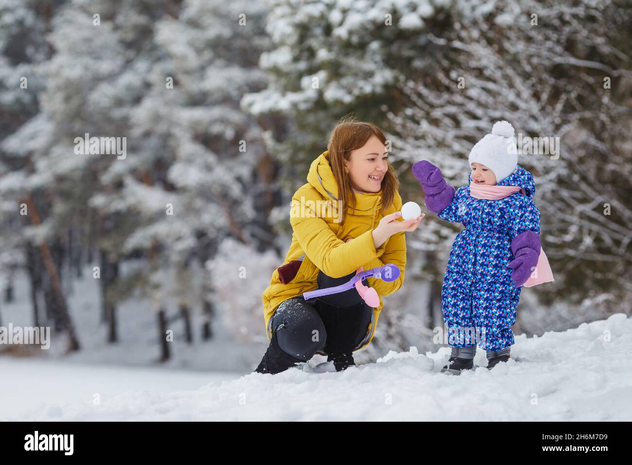 Une jeune femme sculpte des boules de neige avec sa petite fille dans la forêt d'hiver.Mignon enfant dans des vêtements chauds ayant amusement extérieur avec la mère.Maman et fille.Famil Banque D'Images