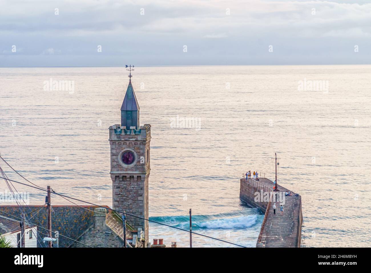 La tour de l'horloge emblématique de Porthleven surplombe le long quai du port alors que les vagues se brisent en dessous, capturées dans une douce lumière du soir pour une scène côtière calme, Cornwall Banque D'Images