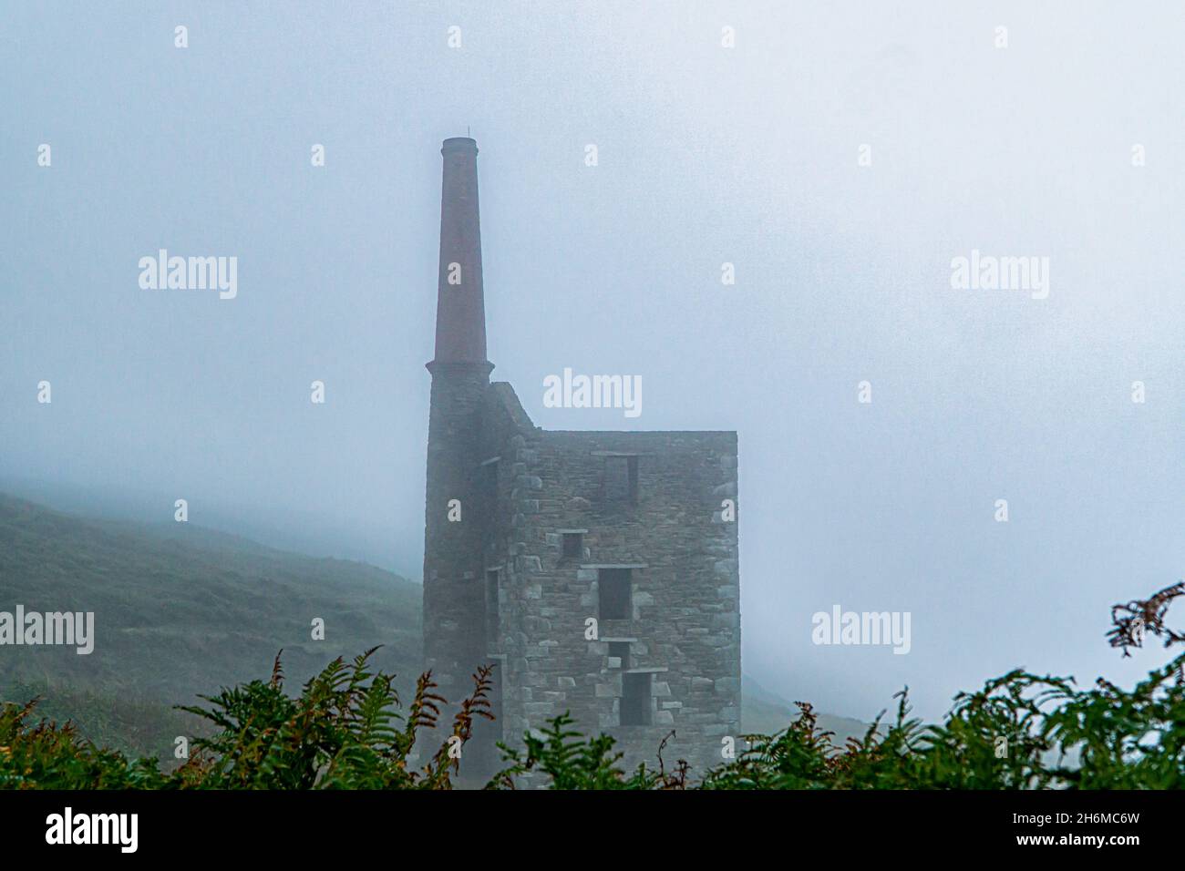 Wheal Prosper Engine House avec une grande cheminée émerge d'un épais brouillard côtier près de Rinsey, Cornwall, Angleterre, créant une scène patrimoniale industrielle sombre Banque D'Images