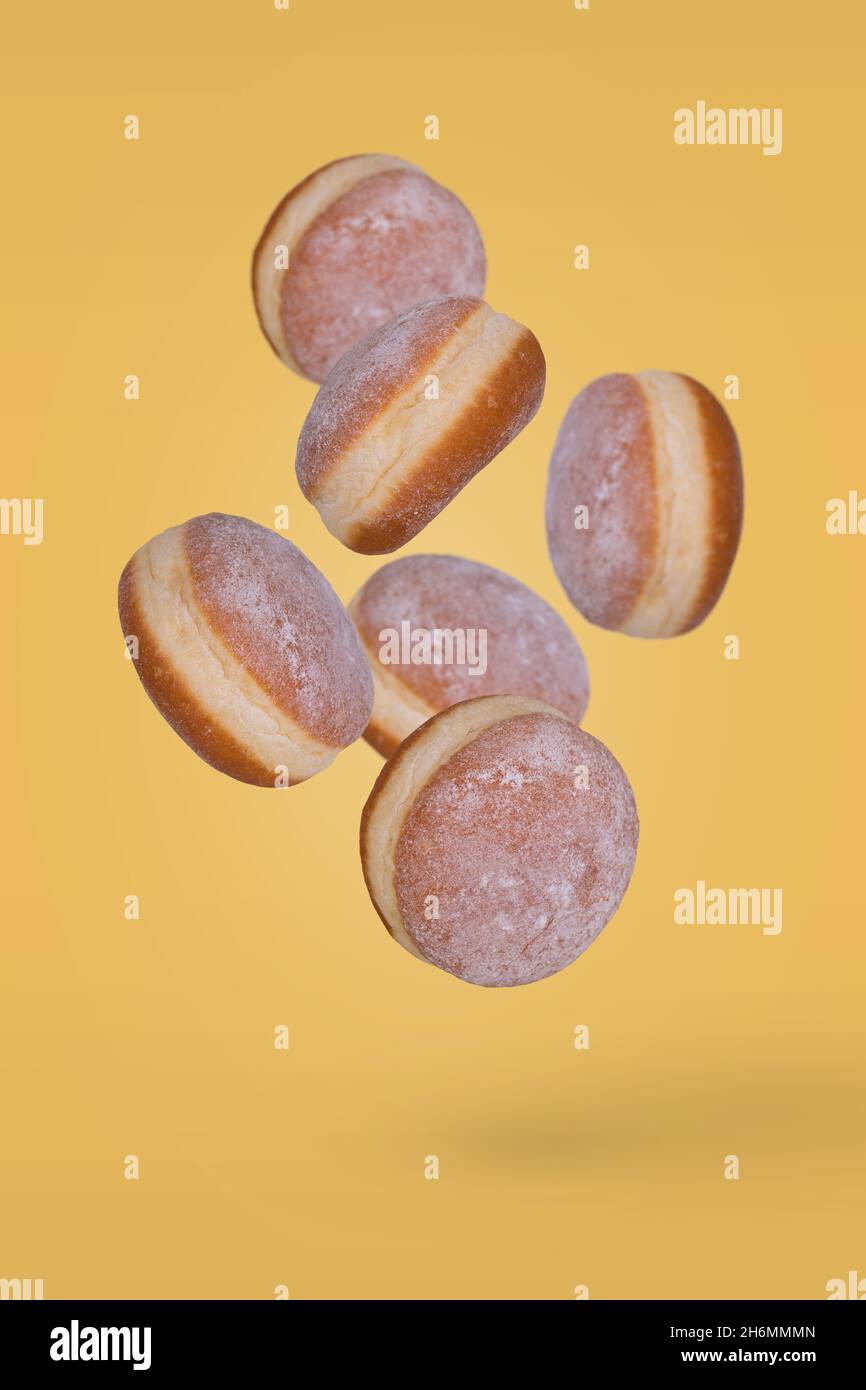 Beignets frais saupoudrés de sucre en poudre volant sur fond jaune.Dessert minimal et concept sucré Banque D'Images