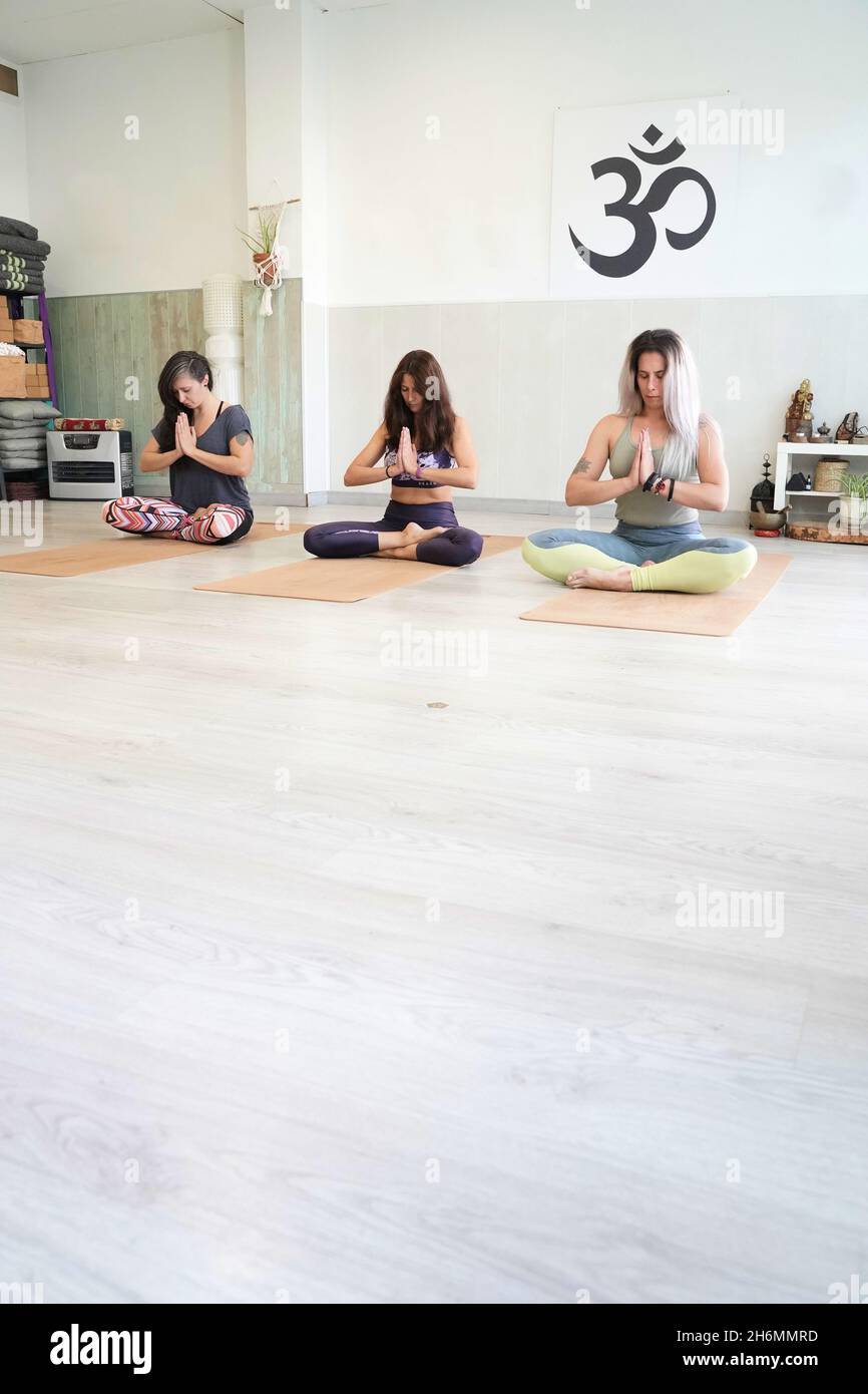 Groupe de jeunes femmes pratiquant un cours de yoga, assis dans les postures de méditation Sukhasana et Siddhasana avec leurs yeux fermés. Banque D'Images