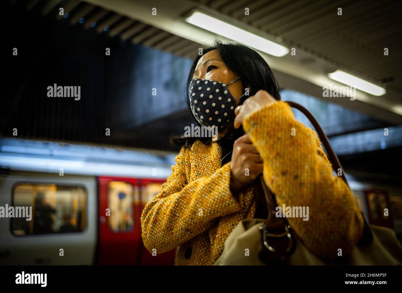 Une femme asiatique portant un masque facial attend un train dans le métro de Londres.Les masques faciaux étaient obligatoires sur le tube en raison du coronavirus Covid-19 Banque D'Images