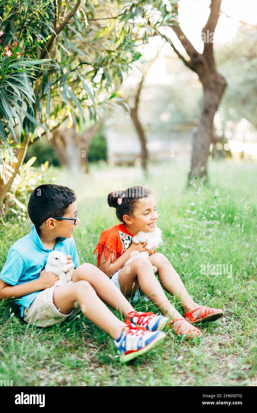 Istanbul, Turquie - 30.05.17: Petit garçon et fille souriant tiennent des lapins blancs dans leurs bras et s'assoient sur l'herbe dans le jardin Banque D'Images