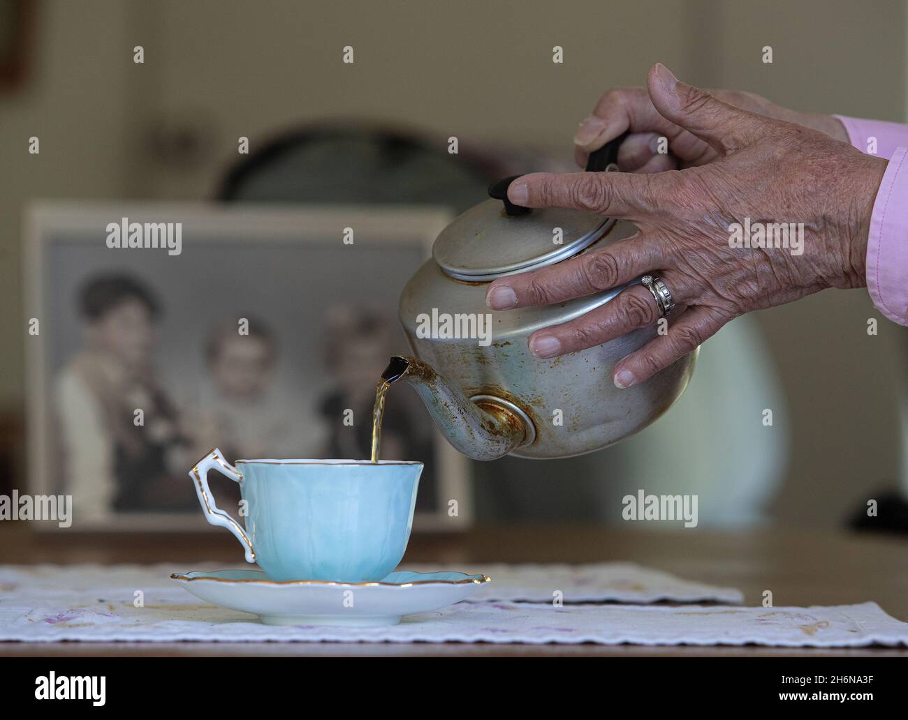 Photo générique d'une vieille main femelle versant une tasse de thé d'un pot dans une tasse de porcelaine. Banque D'Images