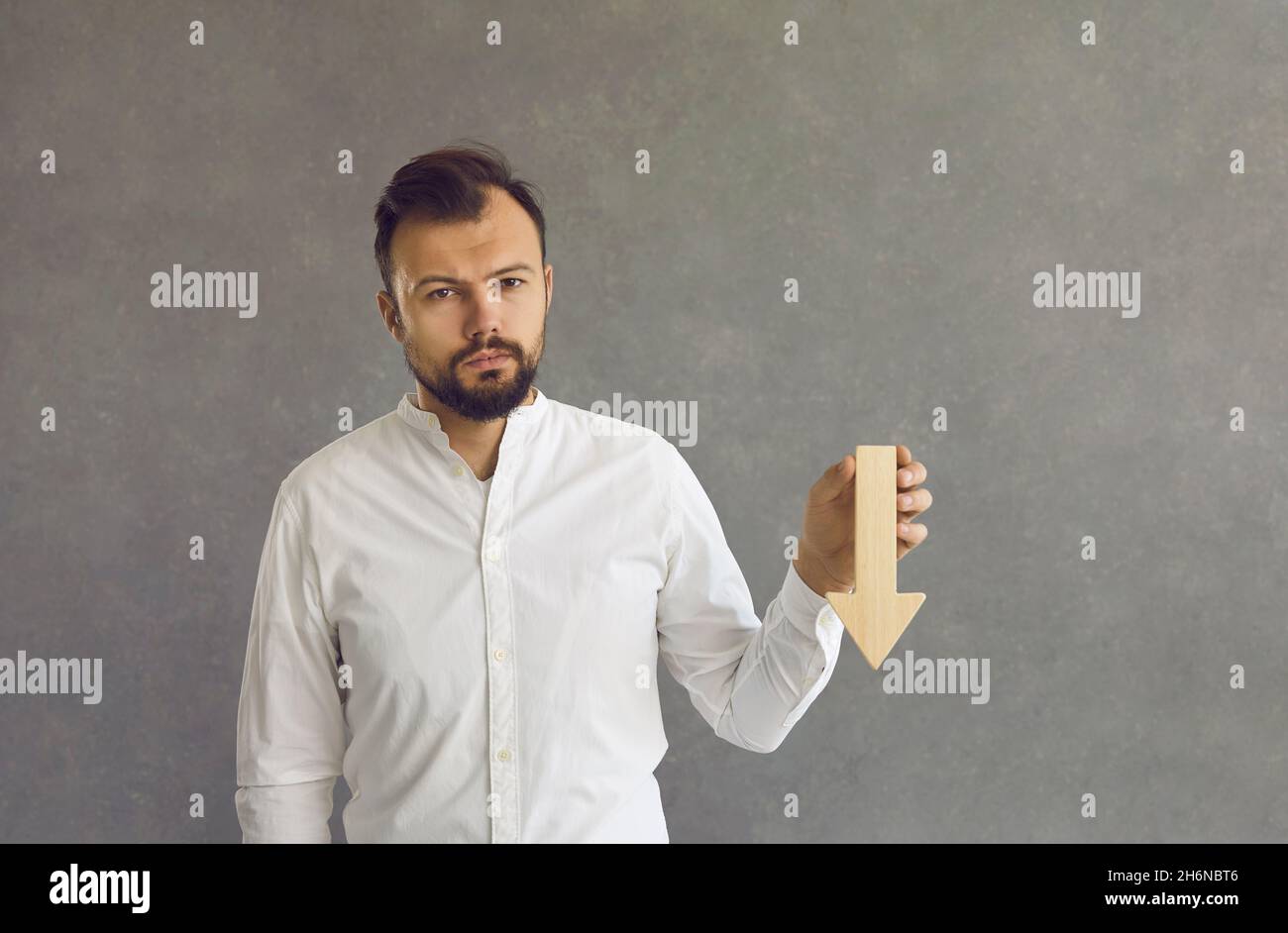 Triste homme d'affaires avec une flèche en bois vers le bas à la main sur le fond du studio Banque D'Images