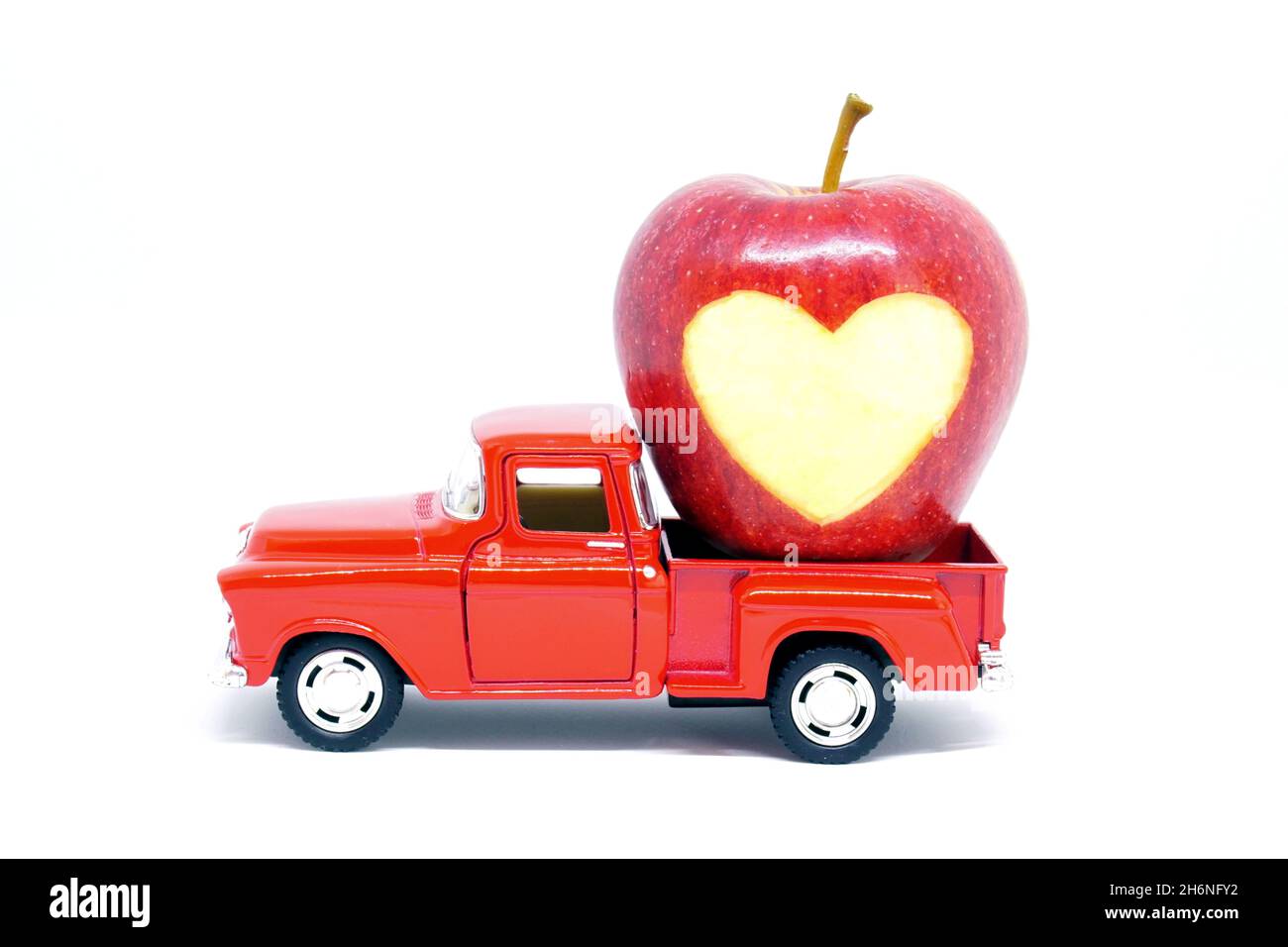 Camion de ramassage de jouets rouges chargé avec une pomme en forme de coeur sculptée, isolée sur fond blanc. Banque D'Images