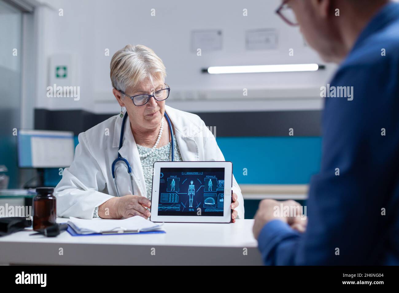 Médecin analysant le comprimé avec l'illustration de l'analyse du corps humain avec l'homme ancien.Un spécialiste de la santé explique le diagnostic au patient malade tout en tenant l'appareil avec une anatomie virtuelle et une expertise Banque D'Images