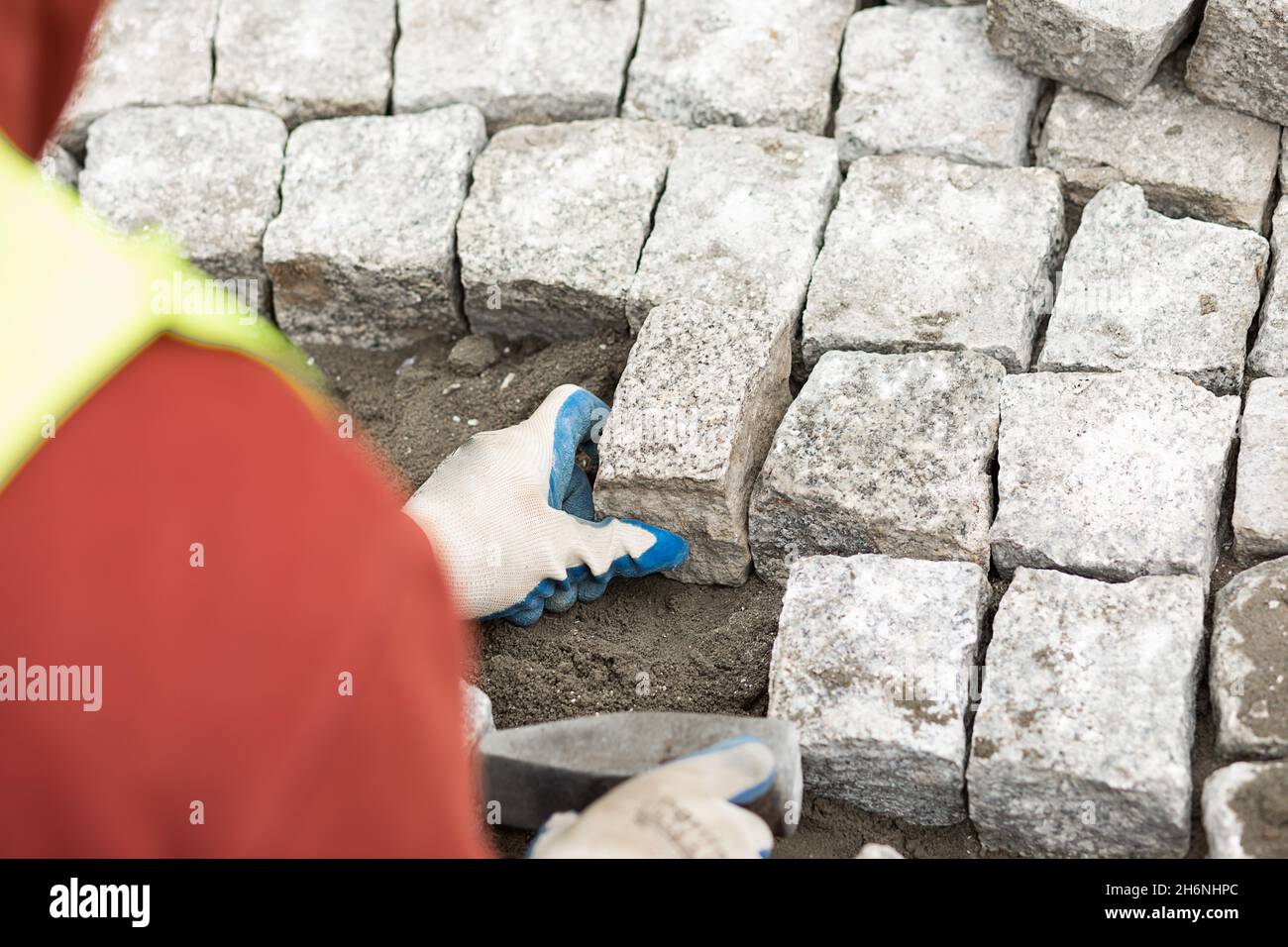 le travailleur a fait le trottoir à partir de briques en utilisant un marteau à la main, au-dessus de la vue d'épaule.Travaux d'entretien sur le pavage avec pavés emboîtés Banque D'Images