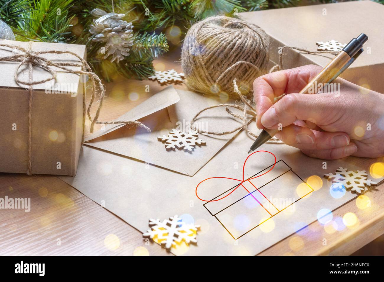 Femme écrivant à la main une lettre de Noël pour le Père Noël, dessinant une boîte cadeau sur la table avec une enveloppe, cadeaux de Noël, sapin et flocons de neige, style écologique, fe Banque D'Images