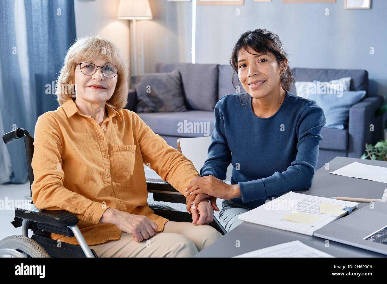 Portrait d'une femme âgée en fauteuil roulant regardant la caméra tout en étant assise dans la pièce avec le personnel soignant à domicile Banque D'Images