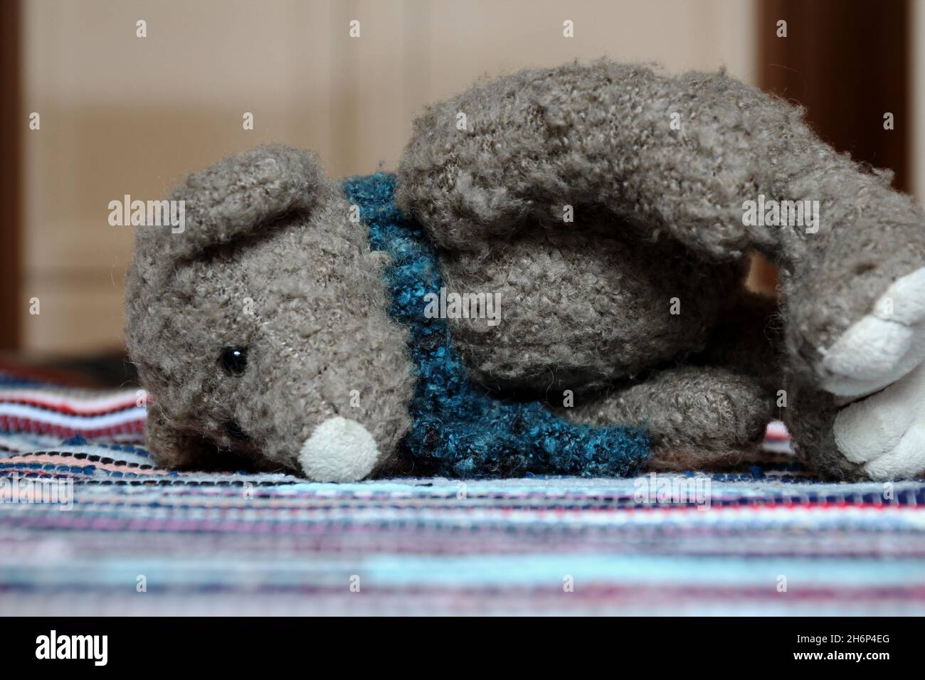Ein Kuscheltier, Teddy, mit einem blauen Schal, liegend auf einem bunten Teppich. Banque D'Images
