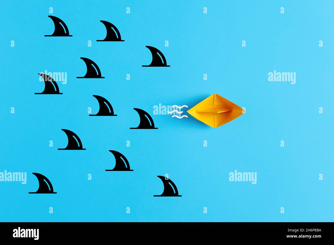 Danger, risque, menace ou complexité de l'entreprise ou concept d'assurance.Les escapades en bateau en papier jaune forment un groupe de requins sur fond bleu. Banque D'Images