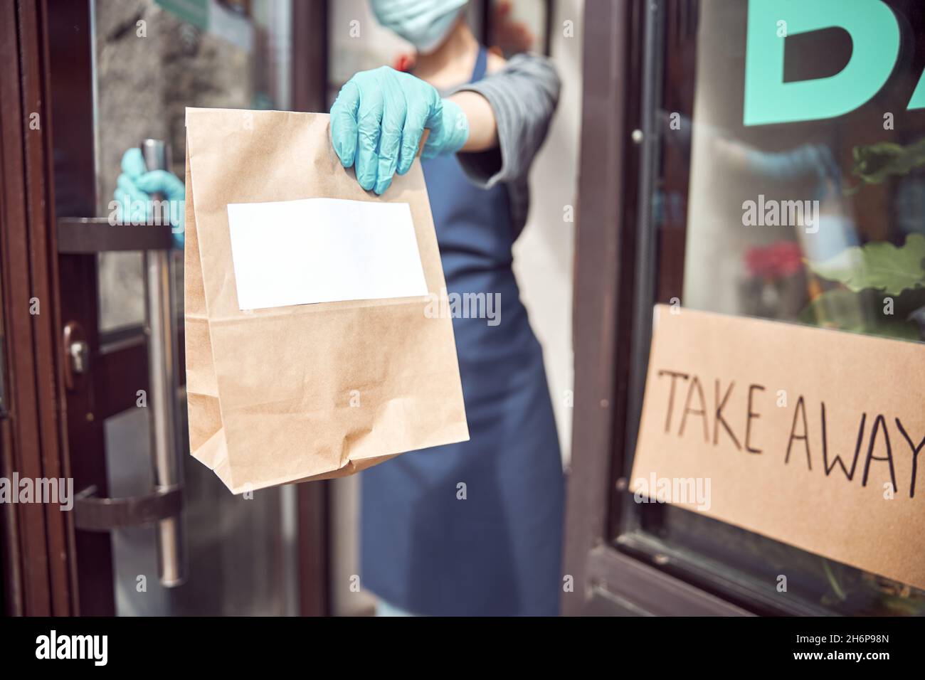 Serveuse sous masque et gants servant des plats à emporter à l'extérieur Banque D'Images