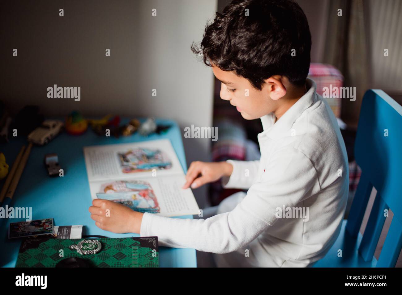 garçon aux cheveux noirs lisant un livre d'histoires à une table Banque D'Images