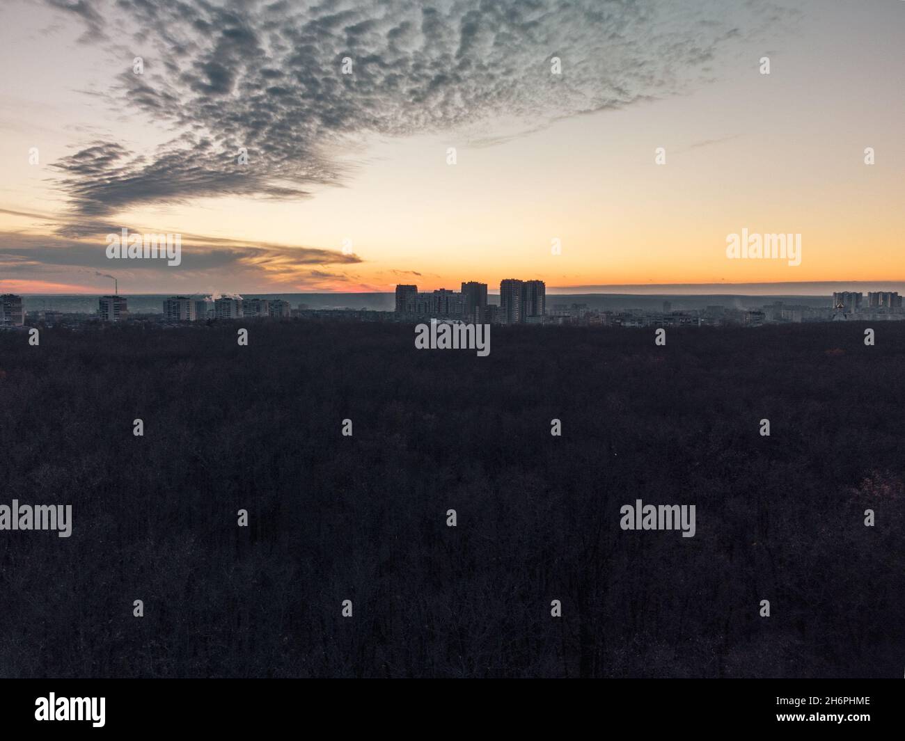 Coucher de soleil vue aérienne en soirée au-dessus de la forêt d'automne sombre près du quartier résidentiel Pavlove Pole dans la ville de Kharkiv.Bâtiments gris à plusieurs étages avec vue panoramique sur oran Banque D'Images