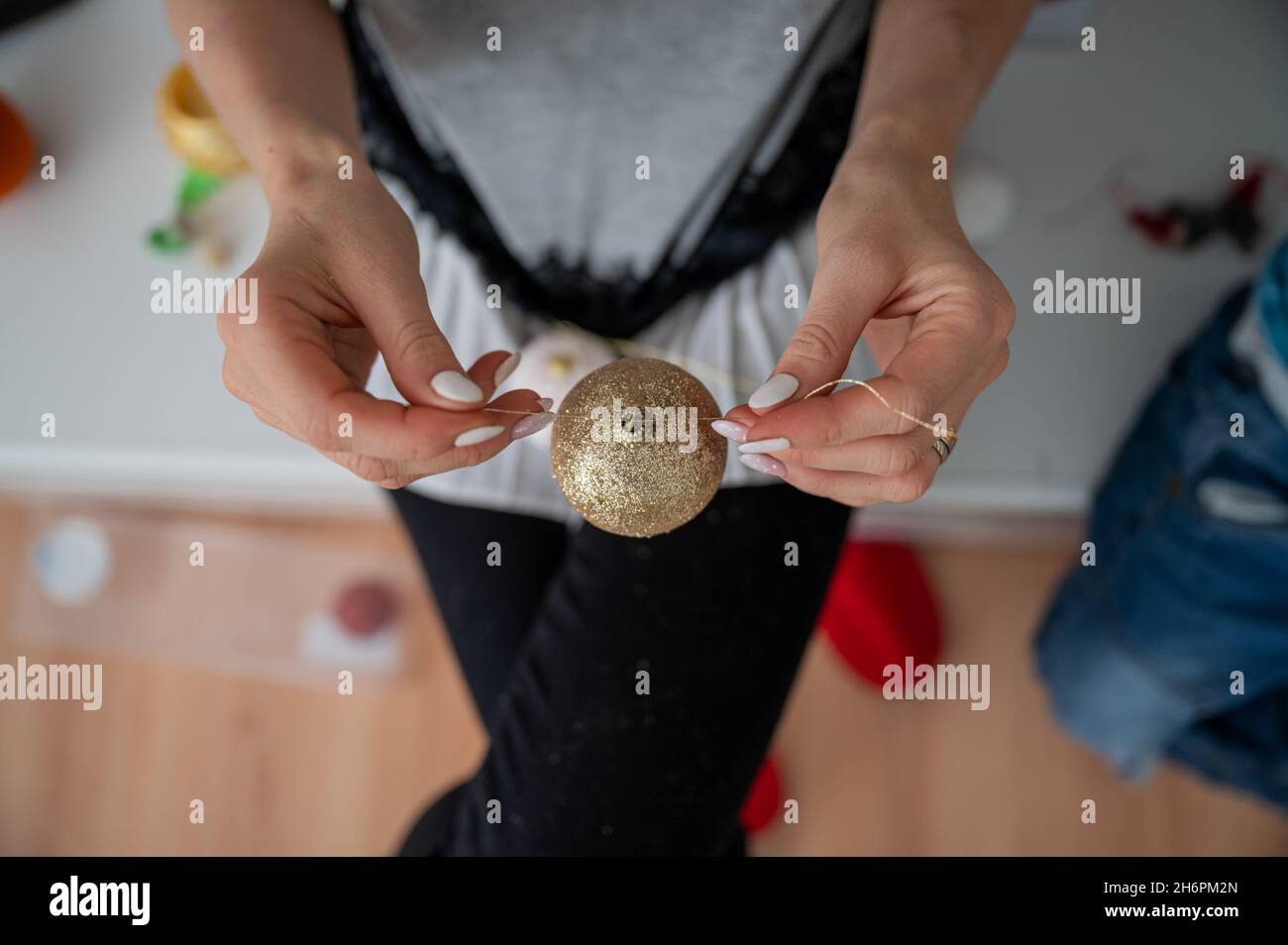 Vue de dessus d'une femme nouant une ficelle dorée à une boule de noël brillante. Banque D'Images