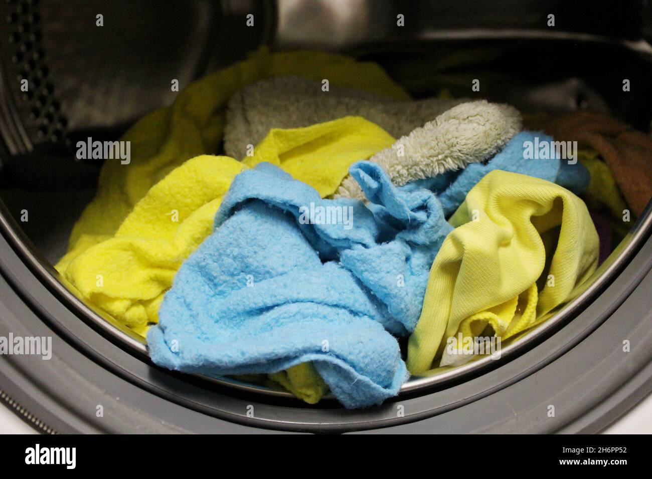 Gewaschene, saubere Putztücher in gelb und blau, die noch in der Waschtrommel der Waschmaschine liegen. Banque D'Images