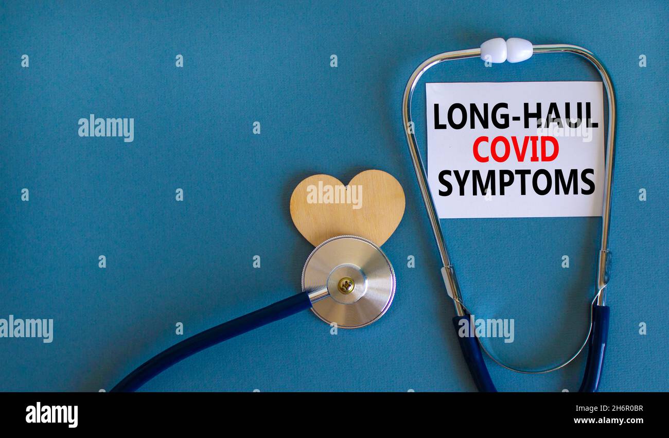 COVID-19 symbole symptômes de covid long-courrier.Carte blanche avec les mots long-haul covid symptômes.Coeur en bois, stéthoscope, fond bleu, espace de copie.Medi Banque D'Images