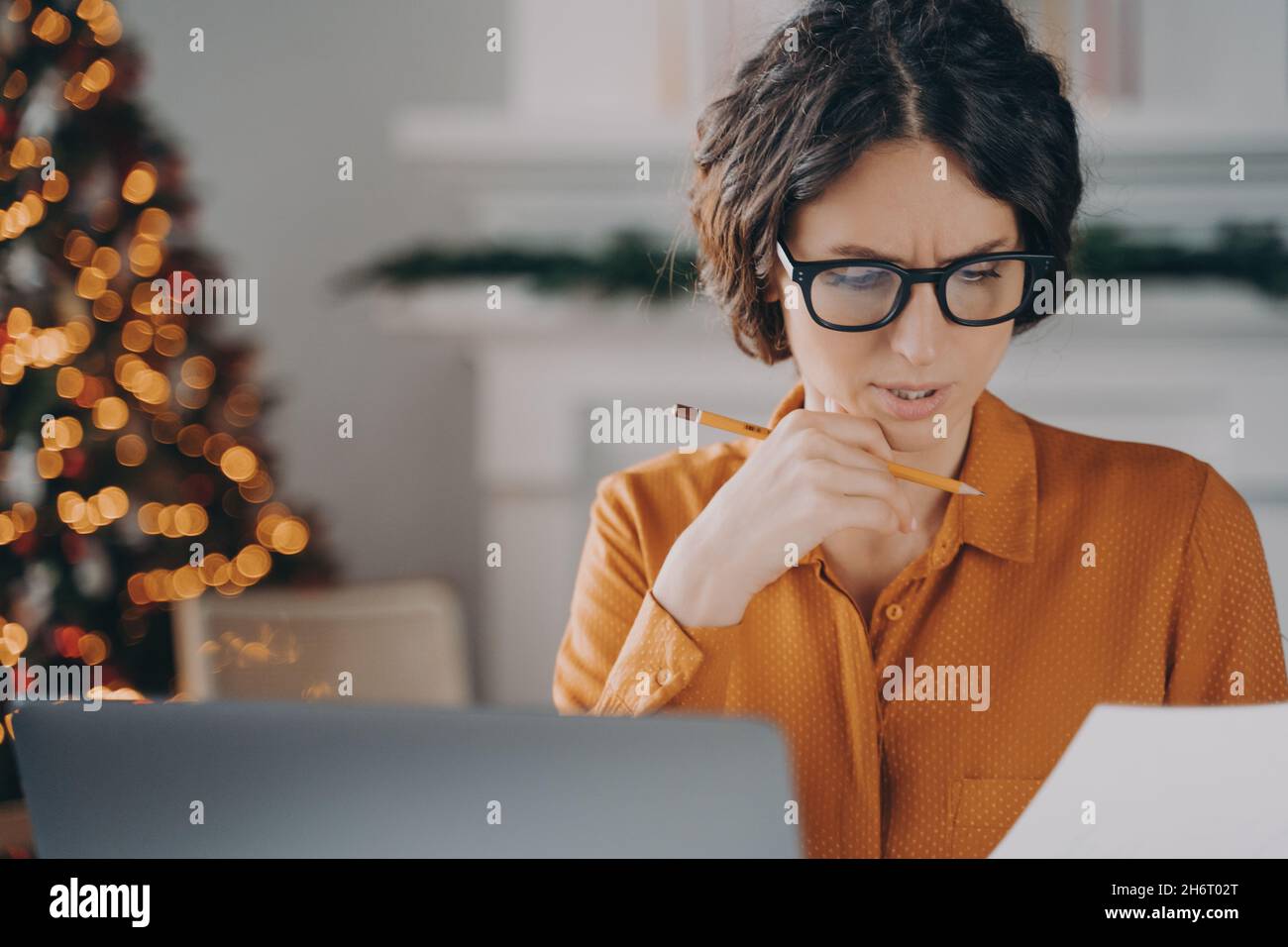 Femme d'affaires attentionnés dans des lunettes travaillant à distance de la maison pendant les vacances de Noël Banque D'Images