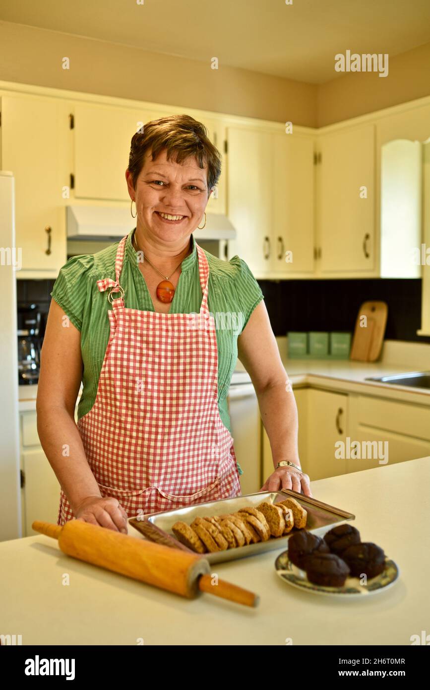 Femme boulangère dans la cuisine maison, portant un tablier et un collier d'ambre, avec des muffins fraîchement cuits et du pain sur le comptoir, Monroe, Wisconsin, États-Unis Banque D'Images