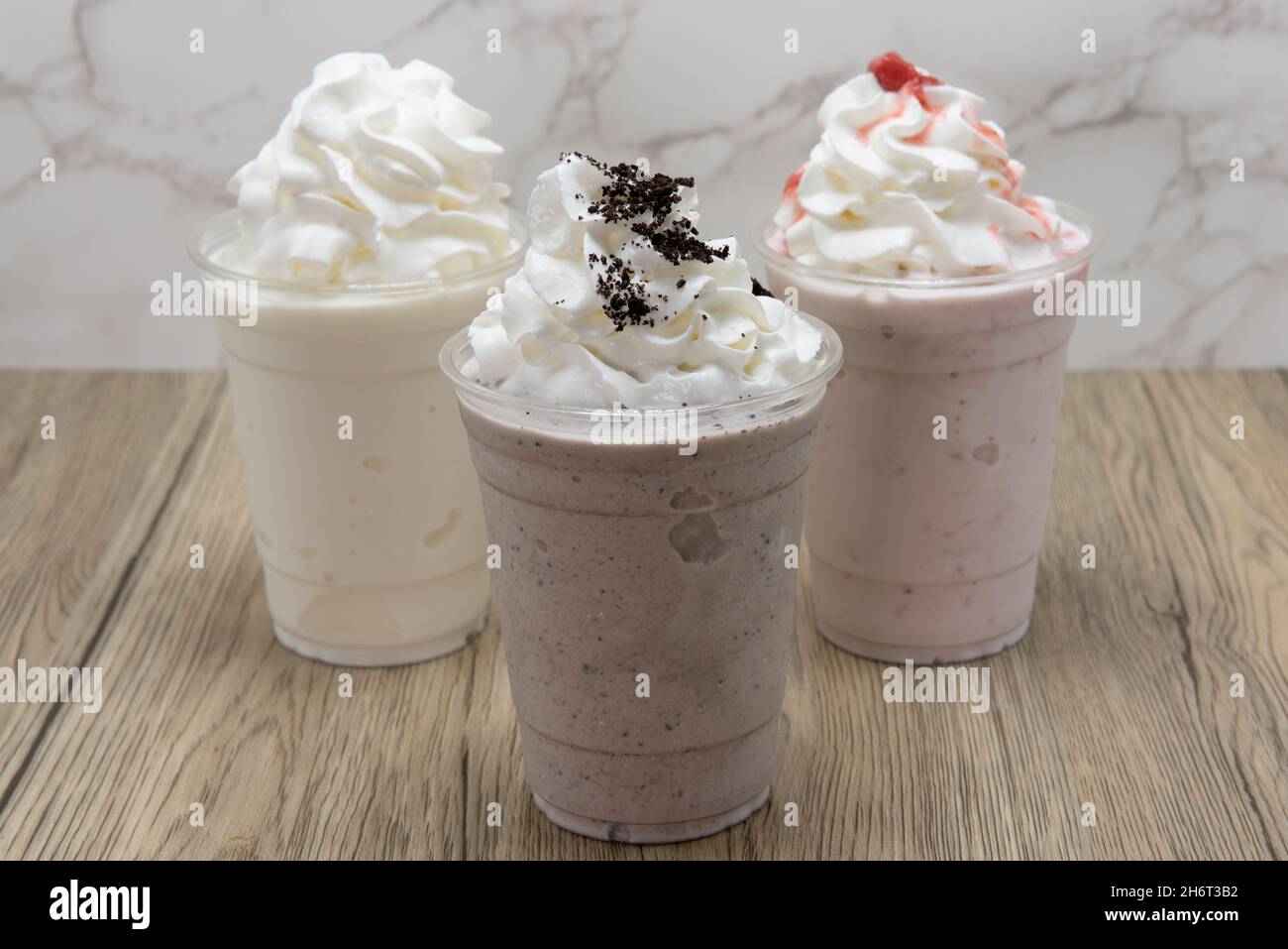 Choix de trois milk-shakes différents servis froids et glatés dans une tasse et nappés de crème fouettée douce. Banque D'Images