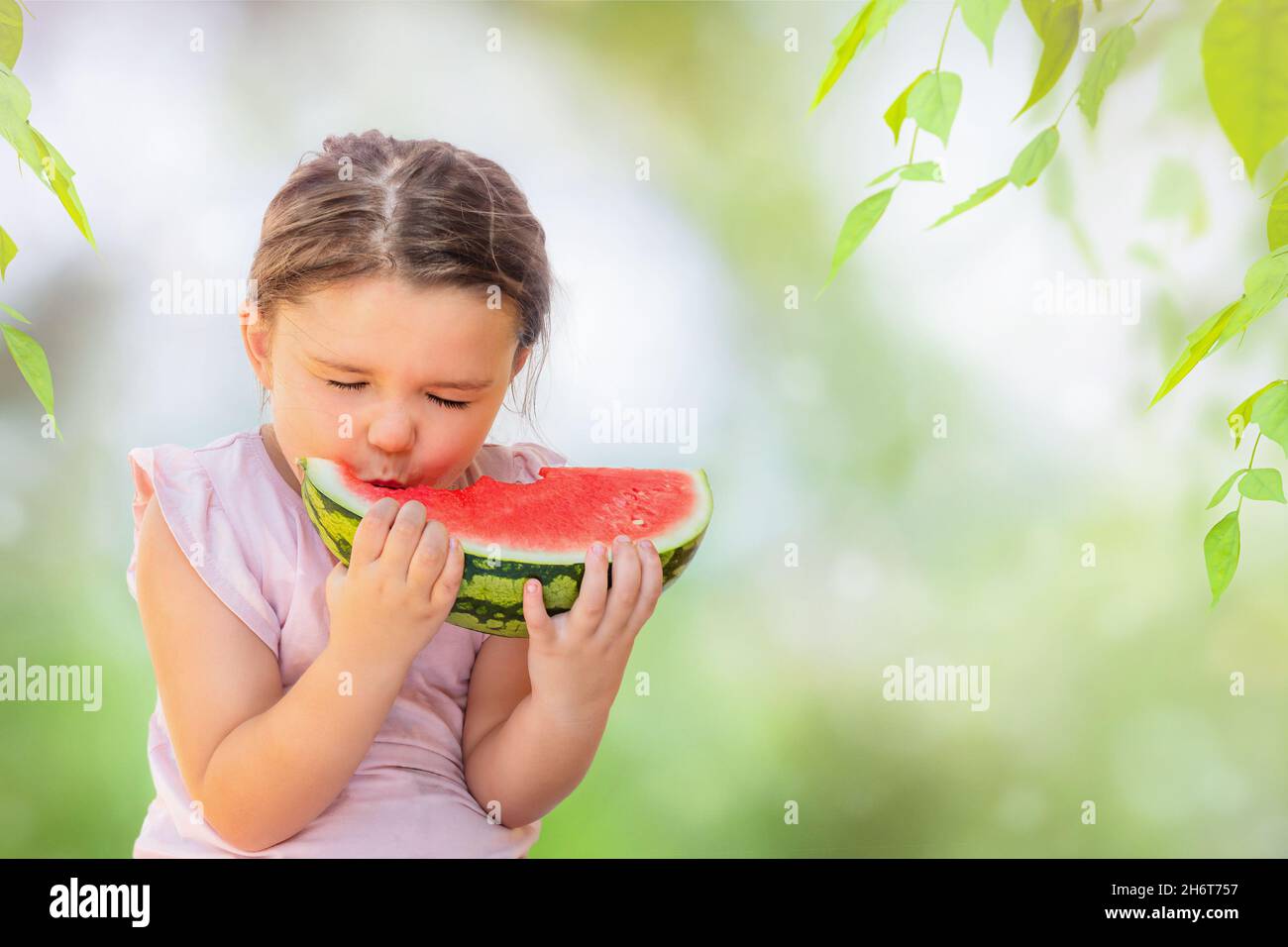 Une fille mord une pastèque rouge juteuse avec un grand plaisir dans l'arrière-cour Banque D'Images