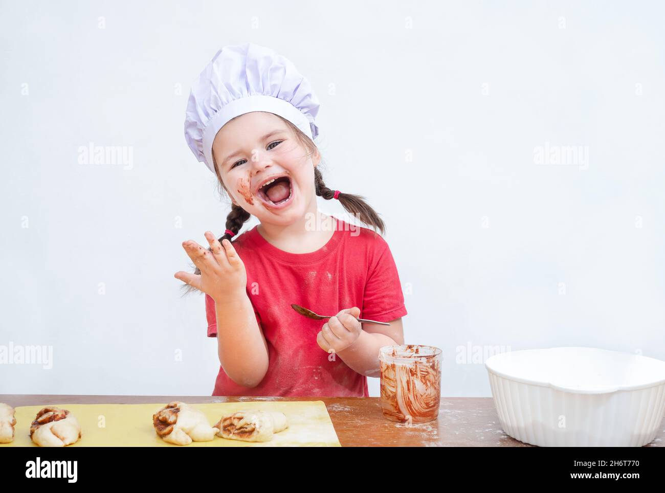 L'enfant dans le chapeau de chef mange une garniture pour la cuisson Banque D'Images