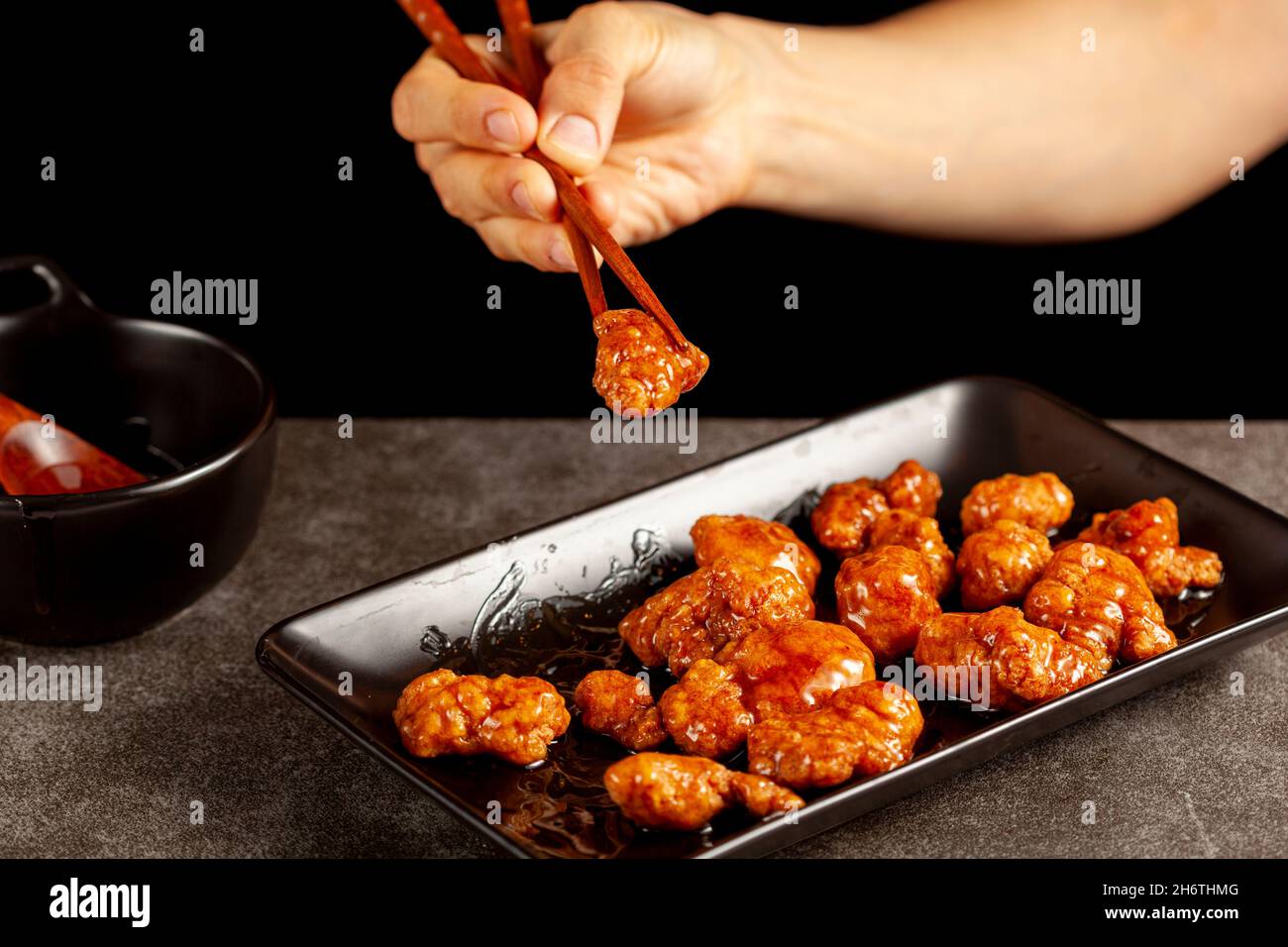 Une personne mange un délicieux poulet mandarin orange, un plat chinois américain à l'aide de baguettes en bois.La sauce est servie dans un bol en porcelaine.Bac foncé Banque D'Images