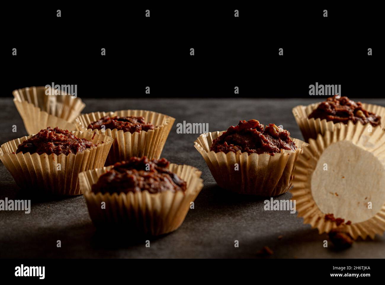 Faible profondeur de champ vue inclinée des muffins au chocolat et aux noix dans les papiers dorsaux sortis du four.Arrière-plan sombre moody image basse lumière.S'émiette Banque D'Images