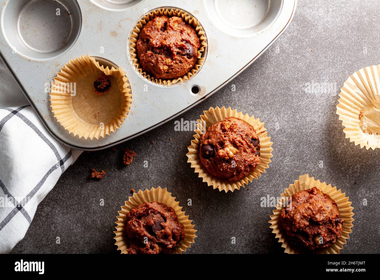 Petits gâteaux au chocolat aux fruits et aux noix dans des sacs et plateau antiadhésif servis frais hors du four pour le petit déjeuner sur un comptoir en pierre.Un chiffon en coton est visible par le Banque D'Images