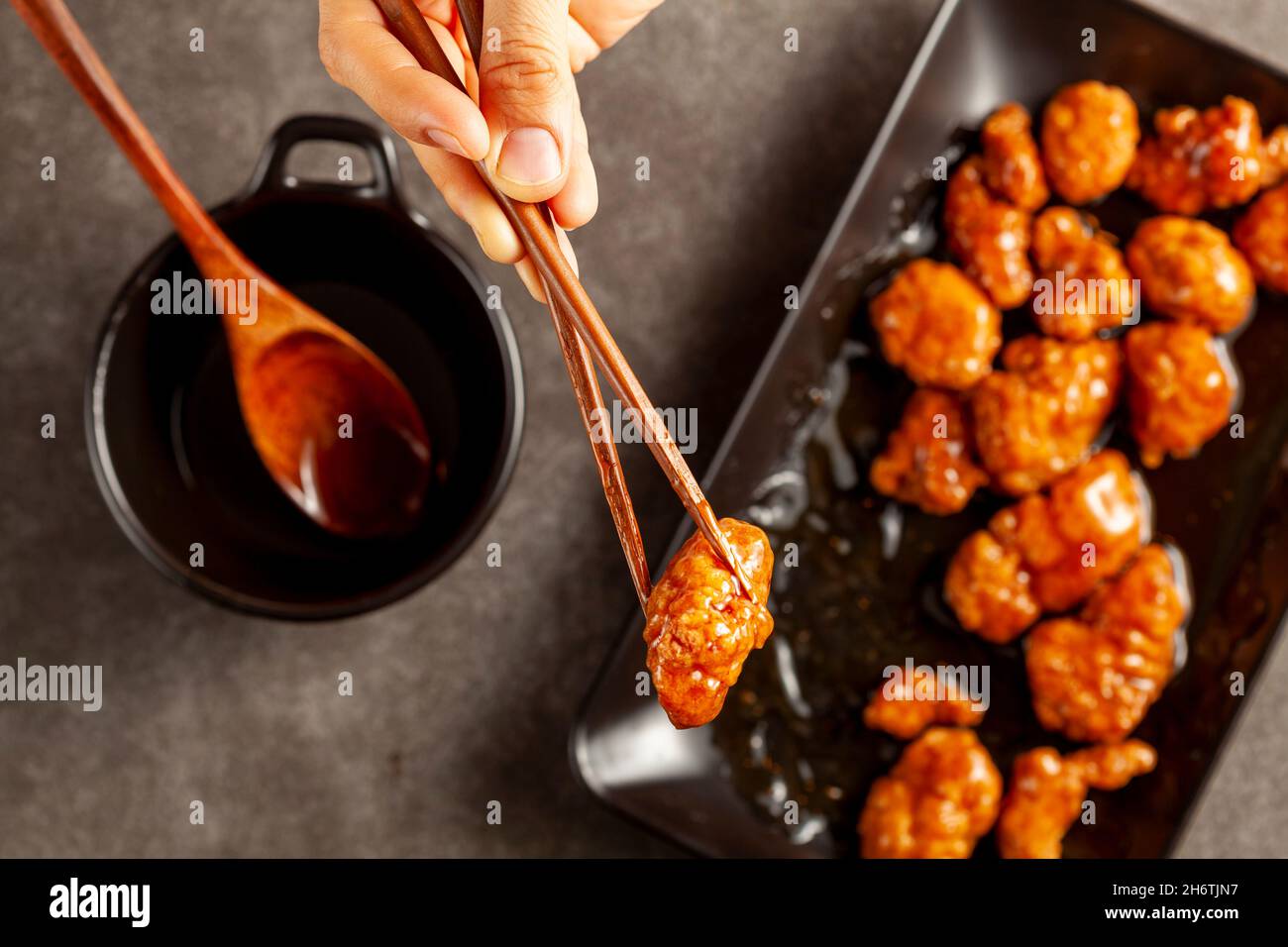 Une personne mange un délicieux poulet mandarin orange, un plat chinois américain à l'aide de baguettes en bois.La sauce est servie dans un bol en porcelaine.Bac foncé Banque D'Images
