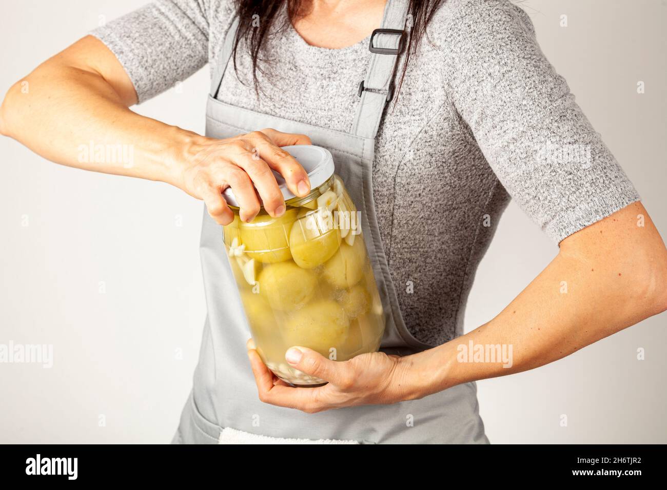 Une femme de cuisine caucasienne portant un tablier tente d'ouvrir un couvercle de pot têtu.Elle utilise la force pour dévisser le couvercle de la cuisine.Image de concept pour le pickling à Banque D'Images