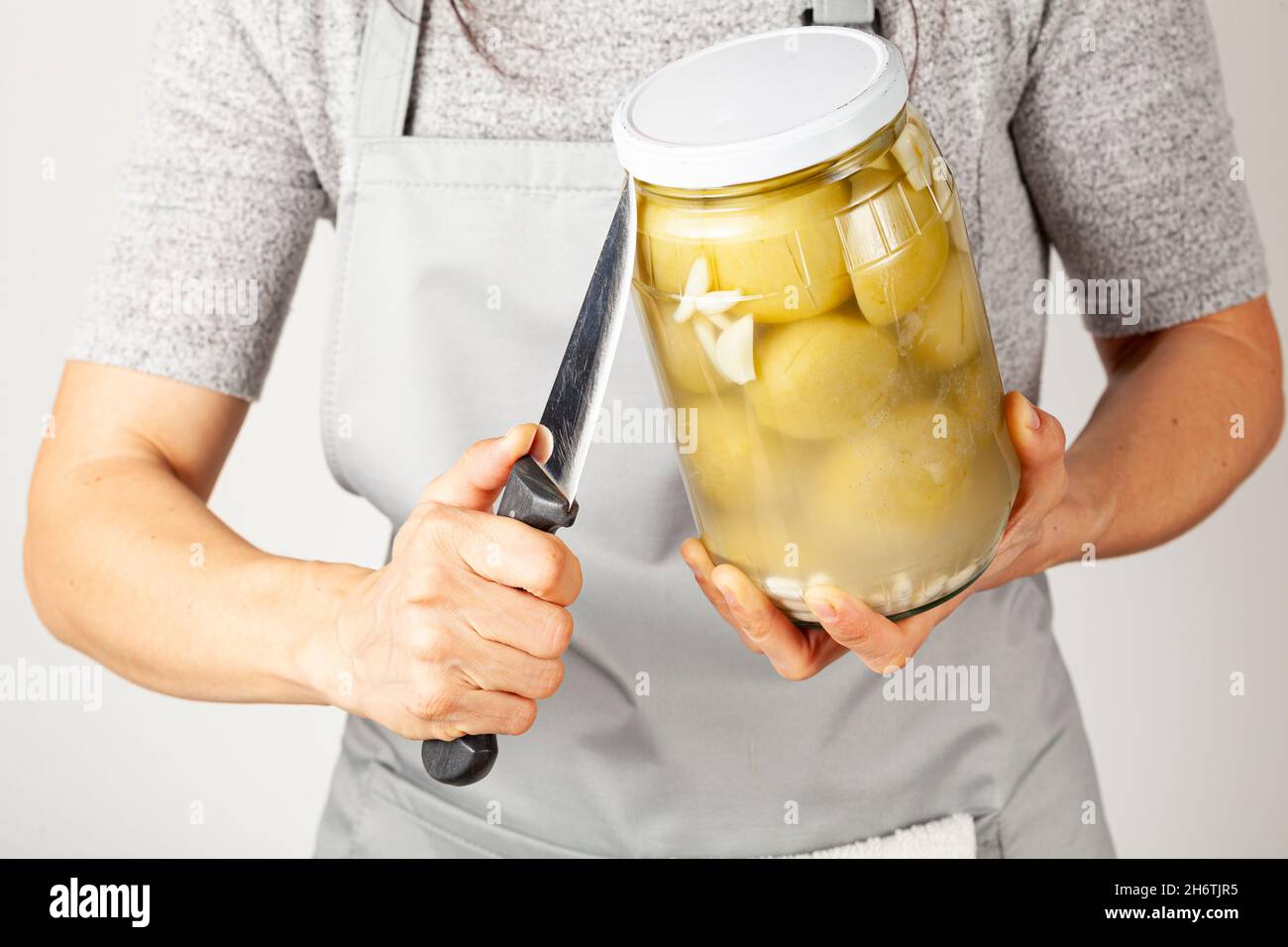 Une femme caucasienne portant un tablier tente d'ouvrir un couvercle têtu.Elle insère un couteau de cuisine tranchant entre le pot et le couvercle pour soulager la pression Banque D'Images